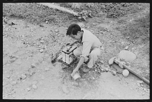 A young boy dipping water from an irrigation ditch, to be brought home for cooking and drinking, in a photo from Chamisal, New Mexico, originally published in July 1940