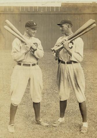 Shoeless Joe Jackson and Ty Cobb face off against each other, each with a handful of bats over one shoulder.